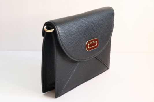 Front View: Black vegan leather envelope style handbag. It has a pebble type texture and gold hardware for the closure and for the cross body straps loops on both sides of the bag